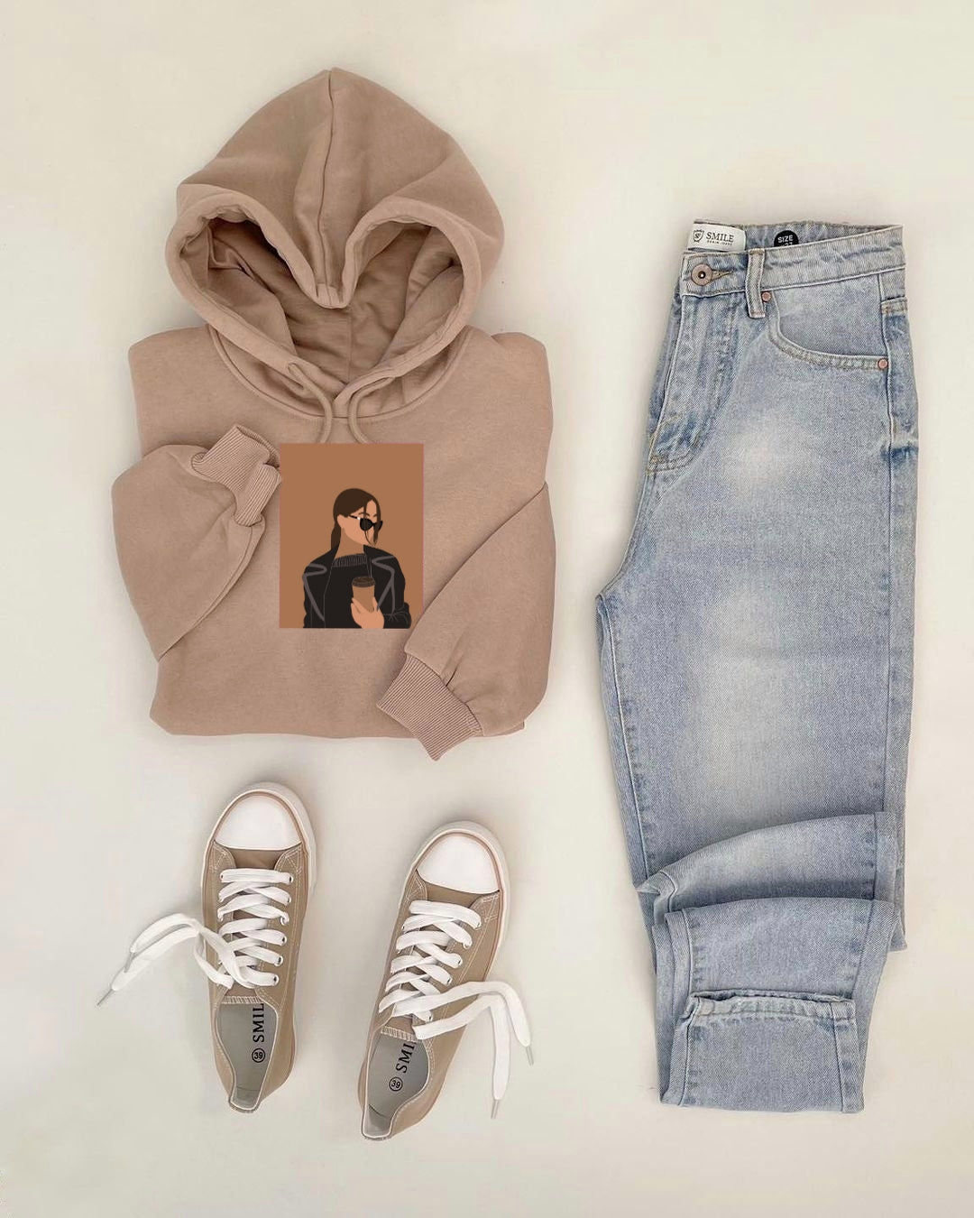 Beige hoodie, light blue jeans, and beige sneakers on a white background