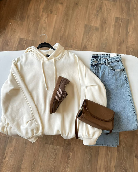 White hoodie, brown Adidas shorts, brown saddle bag, and blue jeans on a white ironing board.
