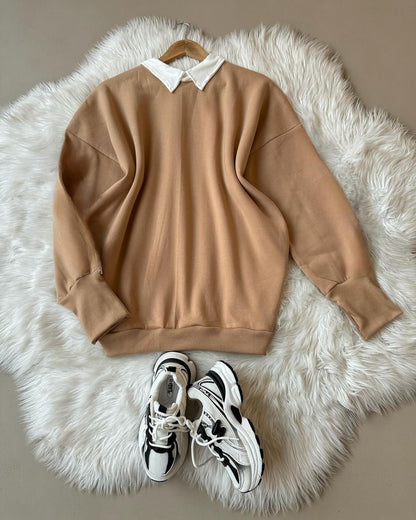 Beige sweatshirt with a white collar on a fluffy white rug, accompanied by black and white sneakers.