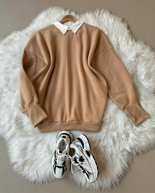 Beige sweatshirt with a white collar on a fluffy white rug, accompanied by black and white sneakers.