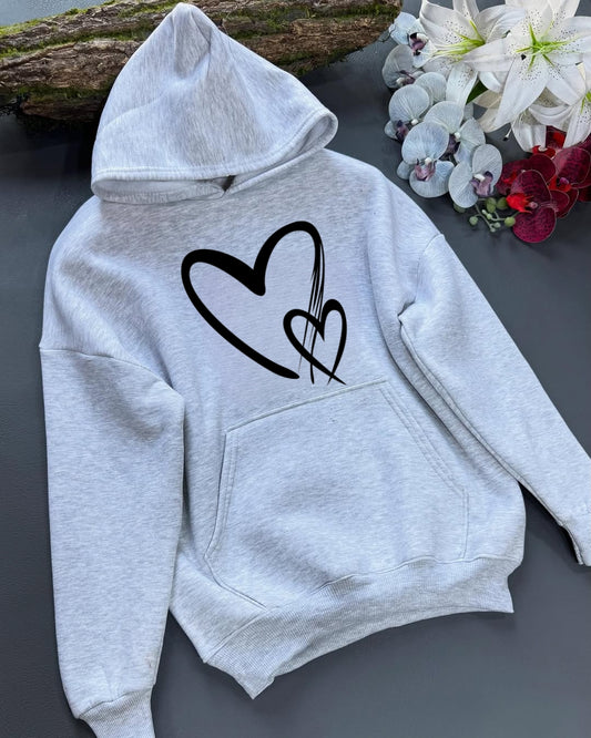 Gray hoodie with a black heart design on a dark surface with flowers in the background