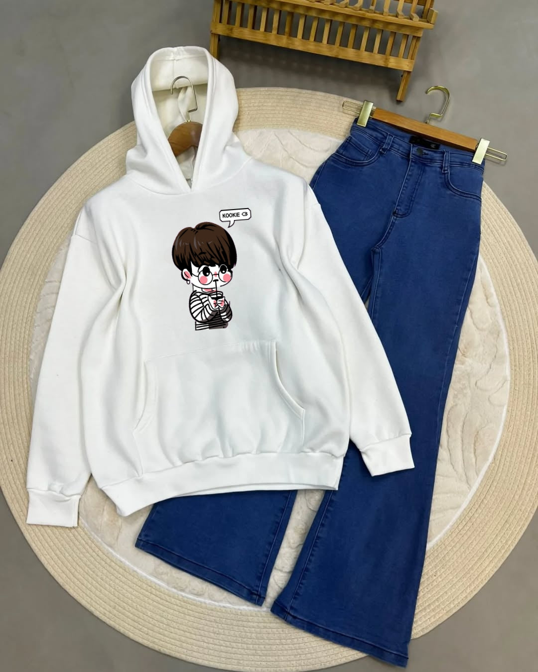White hoodie with cartoon character and blue jeans on a round beige mat